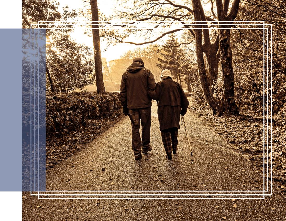 An elderly couple walking together on a tree-lined path
